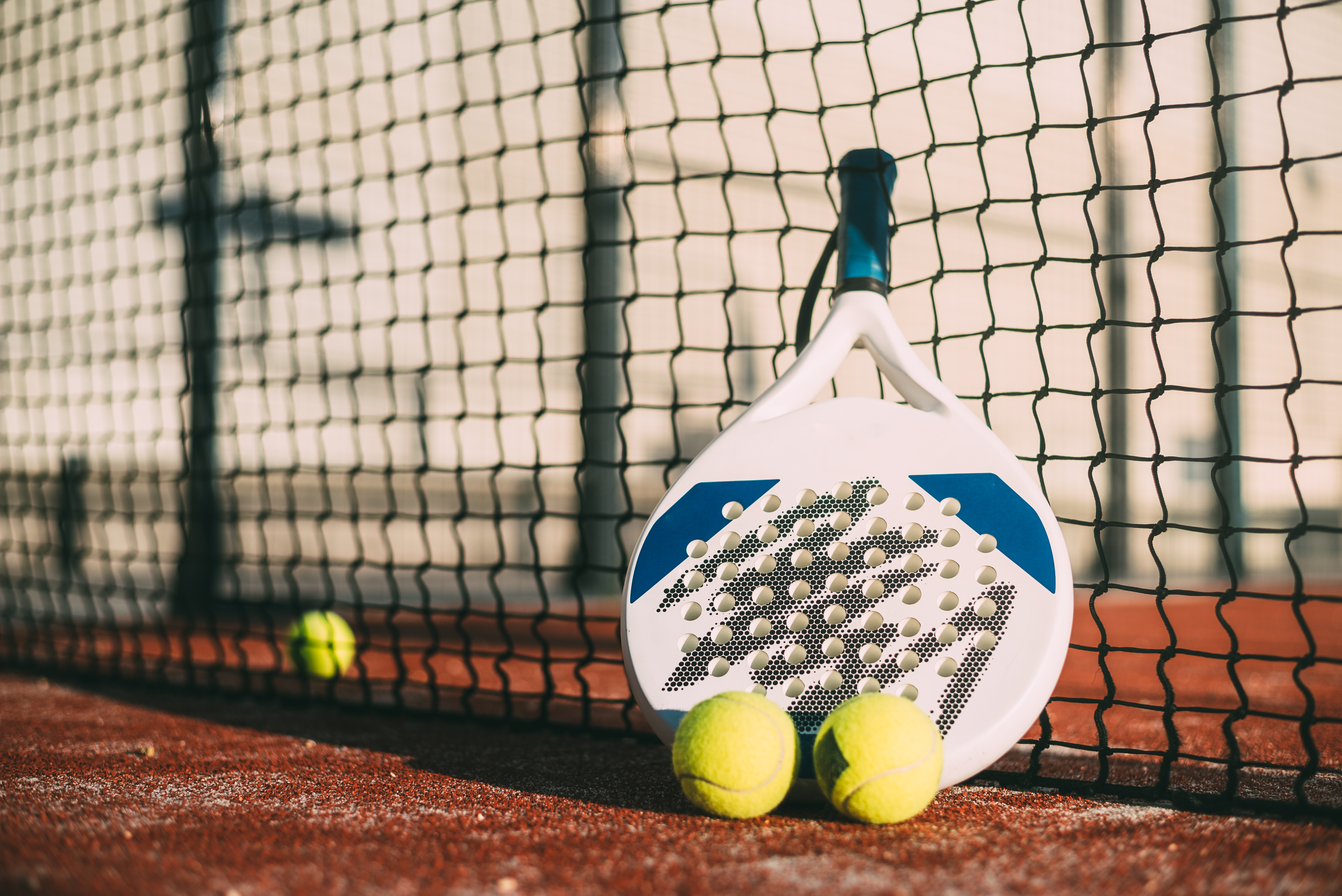 Raquete e bolas de padel apoiadas junto à rede